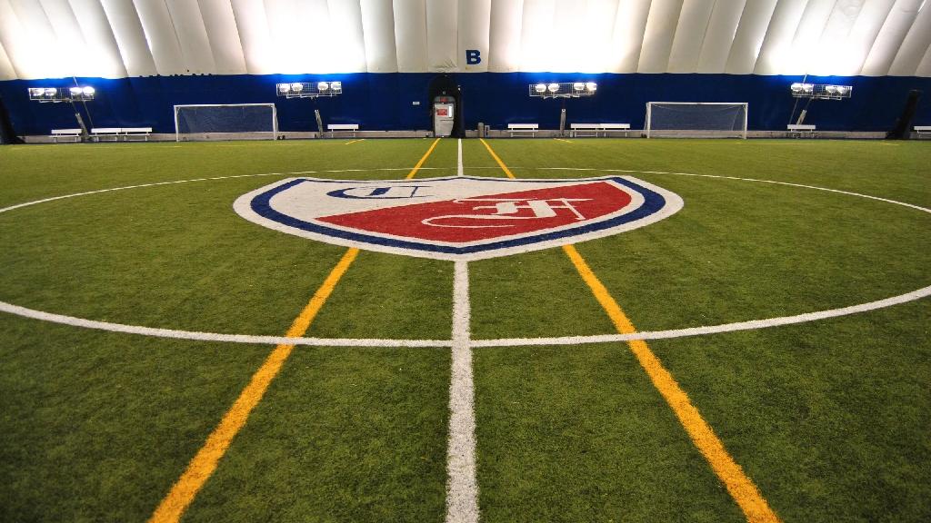 Indoor dome synthetic soccer field at Collège Français featuring center field logo, marked playing lines, goalposts, and bright training lights.