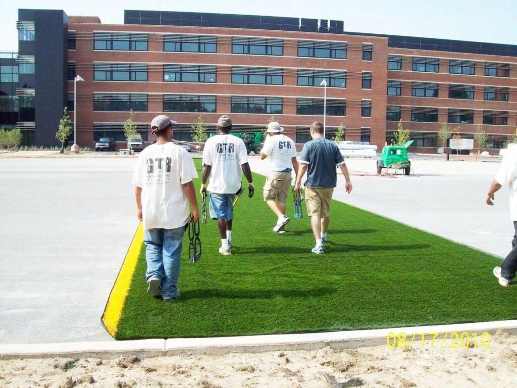 Professional installation team laying commercial artificial grass landscaping on an urban property development site