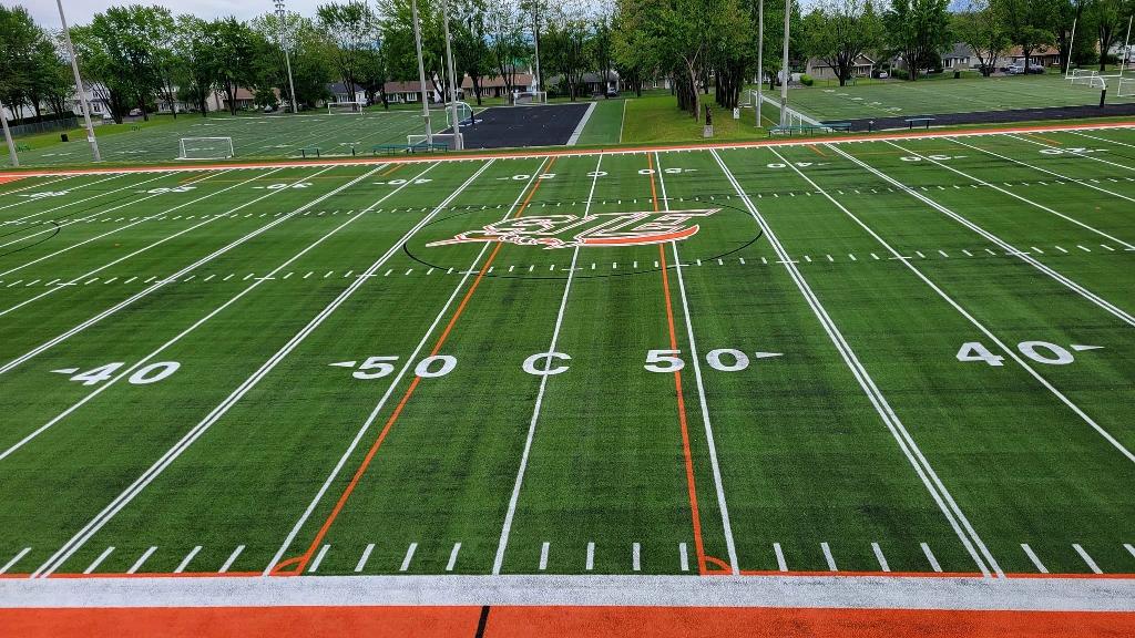 Aerial view of École Secondaire Saint-Jean Eudes synthetic turf sports field with football yard lines, soccer goals, and surrounding trees.