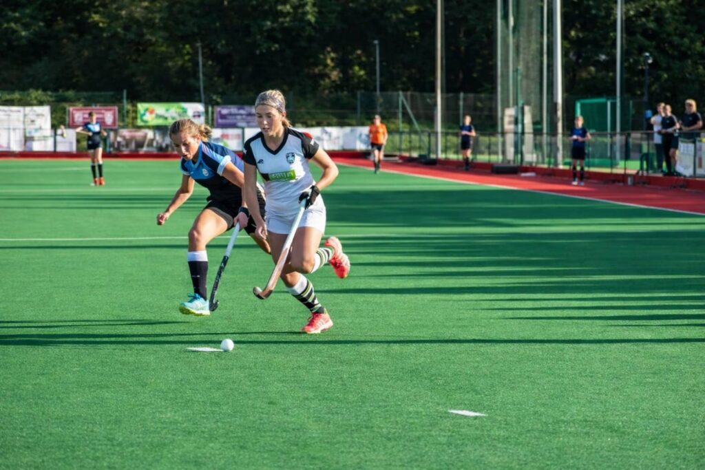 Players competing in a field hockey match on artificial turf field with action in progress