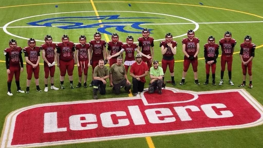 Youth football team and coaches standing on an indoor synthetic turf field with Leclerc logo branding and center field markings.