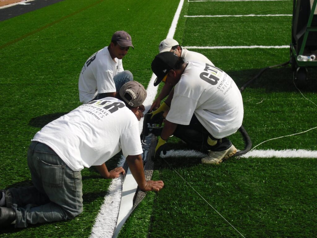GTR Turf installation team working on synthetic grass field seam and line marking during professional sports turf installation.