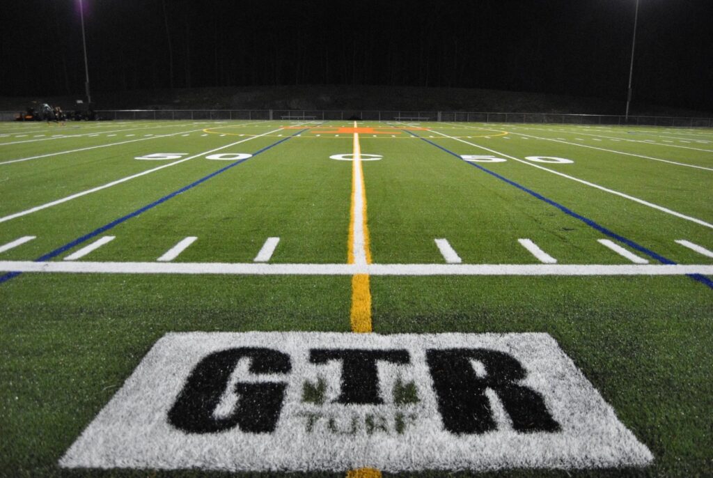 Artificial turf sports field by GTR Turf with football yard lines and illuminated stadium lighting at night