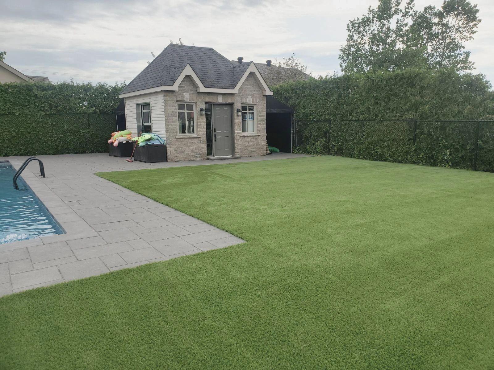 Luxury residential backyard featuring artificial turf lawn, poolside patio, and elegant pool house with landscaped privacy hedges