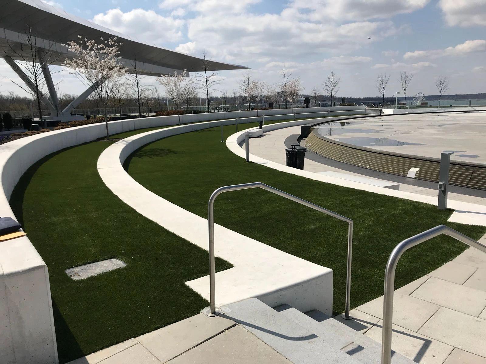 “Modern commercial outdoor space featuring curved artificial turf landscaping, architectural seating walls, and contemporary plaza design